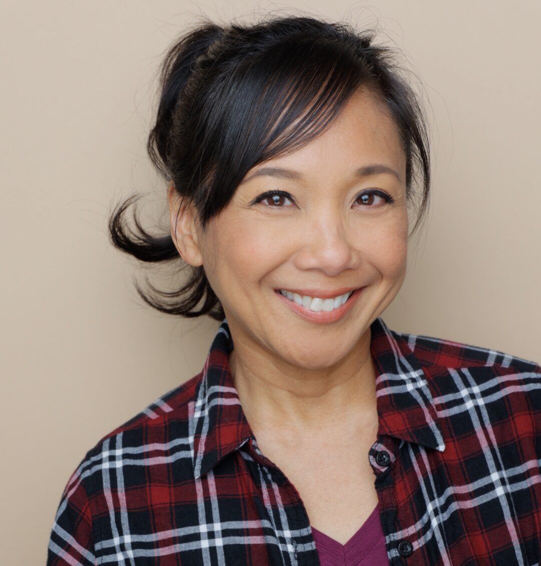 Jennifer Aquino smiling and wearing a red and black plaid shirt over a purple t-shirt.